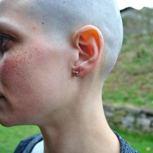 May include: A close-up of a person's face with a shaved head. The person has a small silver earring in their left ear.