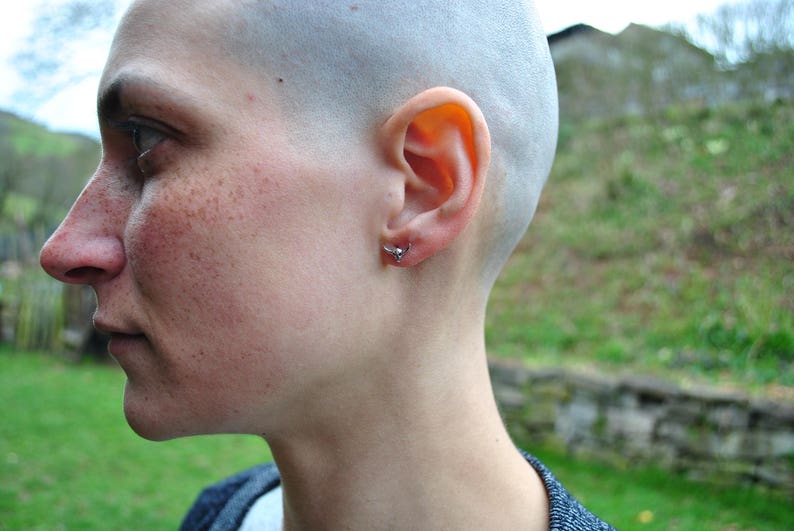 May include: A close-up of a person's face with a shaved head. The person has a small silver earring in their left ear.