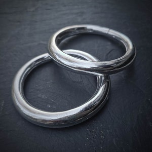 Op de afbeelding: Twee zilveren metalen ringen, een op de andere gestapeld, op een donkergrijze achtergrond.