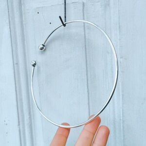 May include: A silver bangle bracelet with two small round balls on the ends.