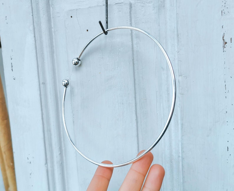 May include: A silver bangle bracelet with two small round balls on the ends.