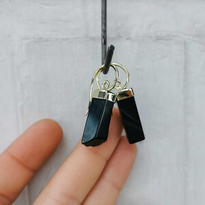 Puede incluir: Un par de pendientes de &oacute;nix negro con detalles dorados. Los pendientes son de forma rectangular y tienen un acabado pulido.