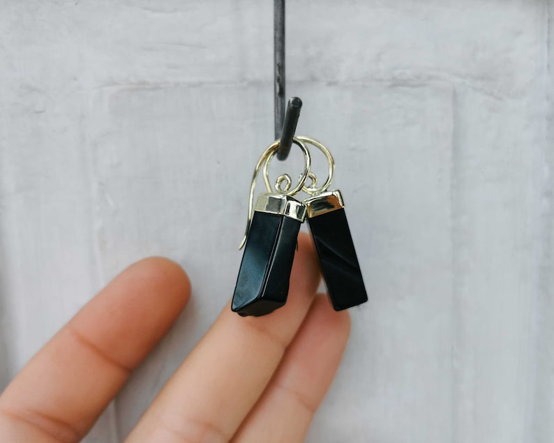 Puede incluir: Un par de pendientes de &oacute;nix negro con detalles dorados. Los pendientes son de forma rectangular y tienen un acabado pulido.