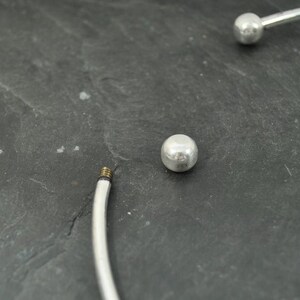 May include: A silver bangle bracelet with two round silver beads. The bracelet is open and has a screw closure.