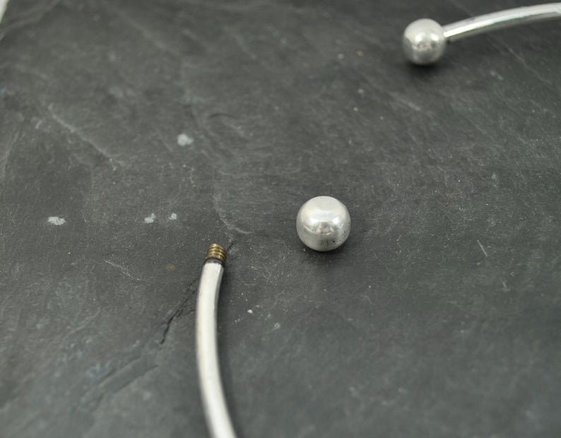 May include: A silver bangle bracelet with two round silver beads. The bracelet is open and has a screw closure.