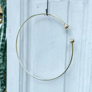 May include: A gold-toned bangle bracelet with two small round balls on the ends.