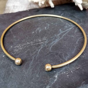 May include: A simple gold bangle bracelet with two round ball ends.