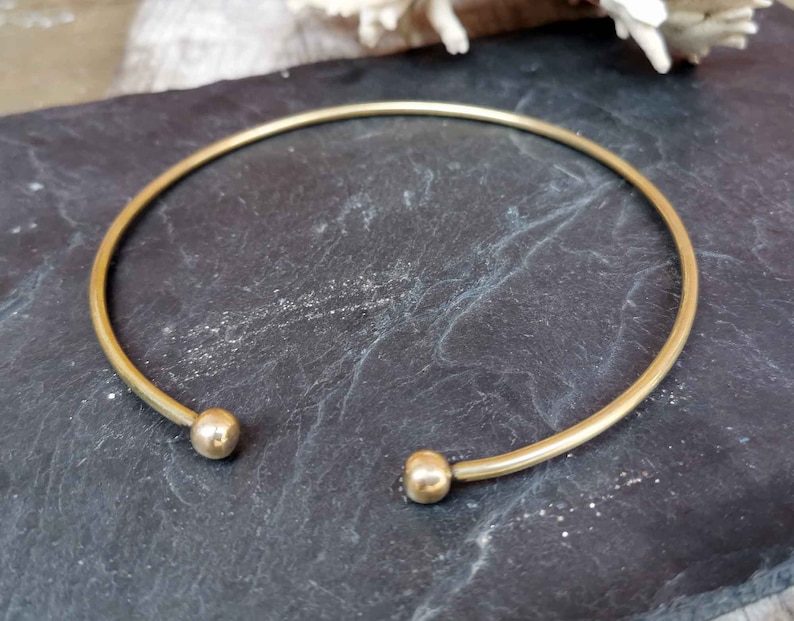 May include: A simple gold bangle bracelet with two round ball ends.