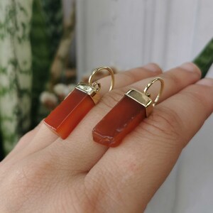 Puede incluir: Un par de pendientes de oro con colgantes de piedra de cornalina naranja. Las piedras son de forma rectangular y tienen un acabado liso y pulido.