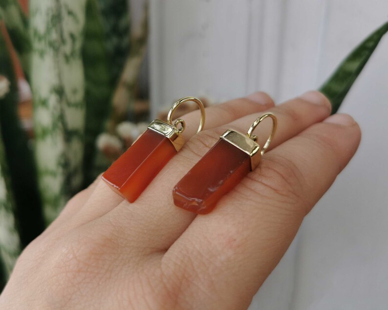 Puede incluir: Un par de pendientes de oro con colgantes de piedra de cornalina naranja. Las piedras son de forma rectangular y tienen un acabado liso y pulido.