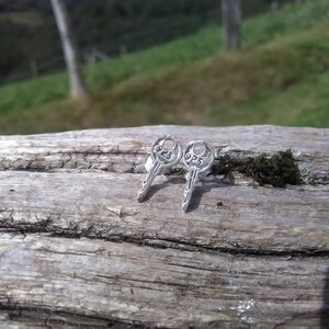 May include: A pair of silver key-shaped earrings with intricate details.