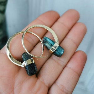 May include: A pair of gold hoop earrings with a dark blue gemstone attached to each hoop.