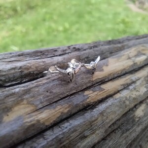 May include: Two silver bull head earrings with a textured finish. The earrings are on a wooden surface.