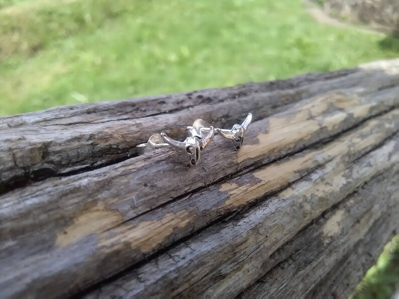May include: Two silver bull head earrings with a textured finish. The earrings are on a wooden surface.