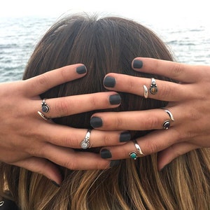 Op de afbeelding: Een close-up van iemands handen met verschillende zilveren ringen met gekleurde edelstenen. De ringen zitten op de wijsvinger, middelvinger en ringvinger.