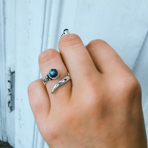 Op de afbeelding: Een zilveren ring met een donkerblauwe edelsteen en een gebogen band. De ring wordt aan een vinger gedragen.