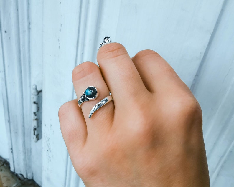 Op de afbeelding: Een zilveren ring met een donkerblauwe edelsteen en een gebogen band. De ring wordt aan een vinger gedragen.