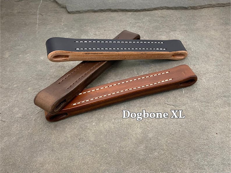 Puede incluir: Tres asas de correa para perro de cuero en diferentes colores y estilos. Las asas est&aacute;n hechas de cuero marr&oacute;n con costuras blancas. El texto "Dogbone XL" es visible en la imagen.
