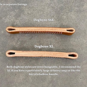 Puede incluir: Dos asas de correa de guitarra de cuero, una etiquetada como "Dogbone Std." y la otra como "Dogbone XL". Ambas asas son marrones y tienen una superficie texturizada. El texto "Both dogbone styles are interchangeable. I recommend the XL if you have a particularly large or heavy amp or like the feel of a bulkier handle." est&aacute; escrito debajo de las asas.