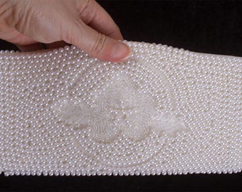 May include: A white clutch purse made entirely of pearls. The pearls are sewn together to create a smooth, textured surface.