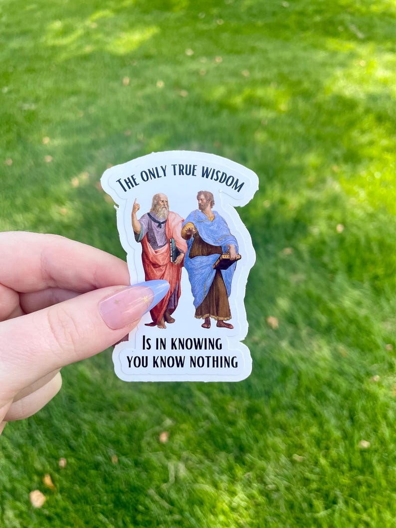 May include: White sticker with a black border featuring an illustration of two men, one pointing to the sky and the other holding a book. The text reads "The only true wisdom is in knowing you know nothing."