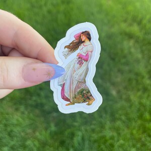 May include: A sticker featuring a vintage illustration of a woman in a flowing white dress with pink accents, holding a bouquet of flowers. The sticker has a white border and is on a green background.