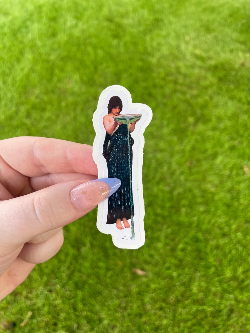 May include: A sticker featuring a painting of a woman in a blue dress holding a bowl with water pouring out.