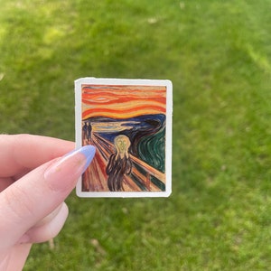 May include: A sticker featuring a reproduction of Edvard Munch's famous painting "The Scream". The painting depicts a figure with a distorted face screaming against a swirling, blood-red sky.