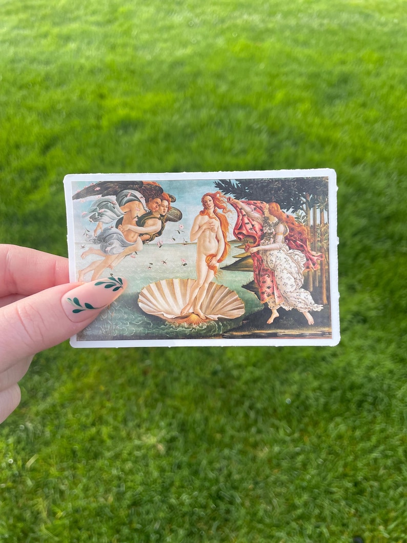 May include: A vintage postcard featuring a painting of the Birth of Venus by Sandro Botticelli. The painting depicts a nude woman standing on a giant scallop shell, with the wind blowing her hair and a flowing drapery behind her. Two winged figures are shown in the background, one holding a red cloak and the other holding a flower.