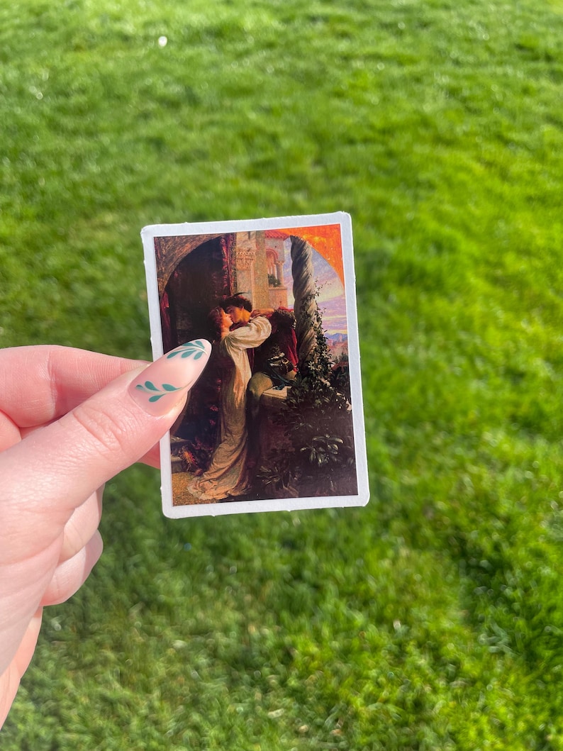 May include: A vintage sticker featuring a painting of a couple embracing in a romantic setting. The woman is wearing a white dress and the man is wearing a red and black outfit. The background is a lush garden with a stone wall and a vine-covered trellis.