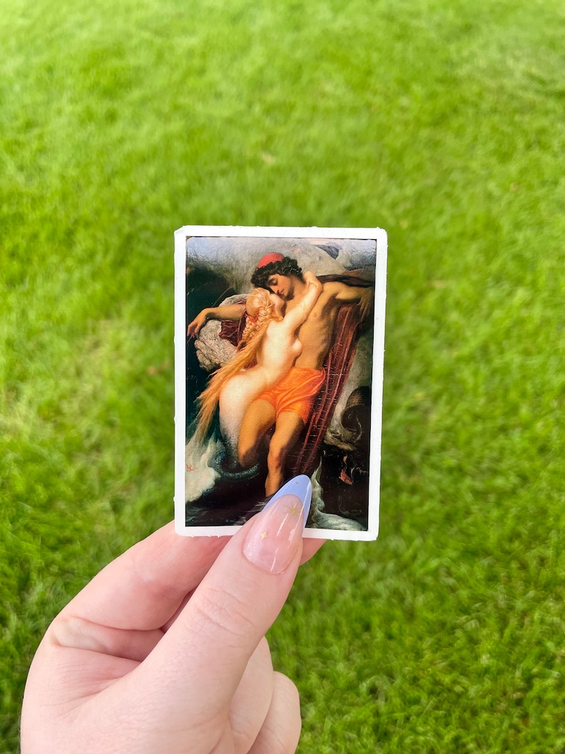 May include: A sticker featuring a painting of a couple embracing. The man is wearing a red hat and the woman is wearing a white dress. The painting is set against a dark blue background with waves and a boat.