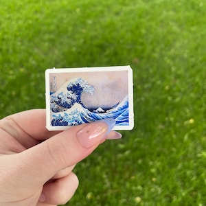Op de afbeelding: Een sticker met een blauwe en witte afbeelding van de Grote Golf voor Kanagawa, een beroemde Japanse houtsnede van Hokusai.