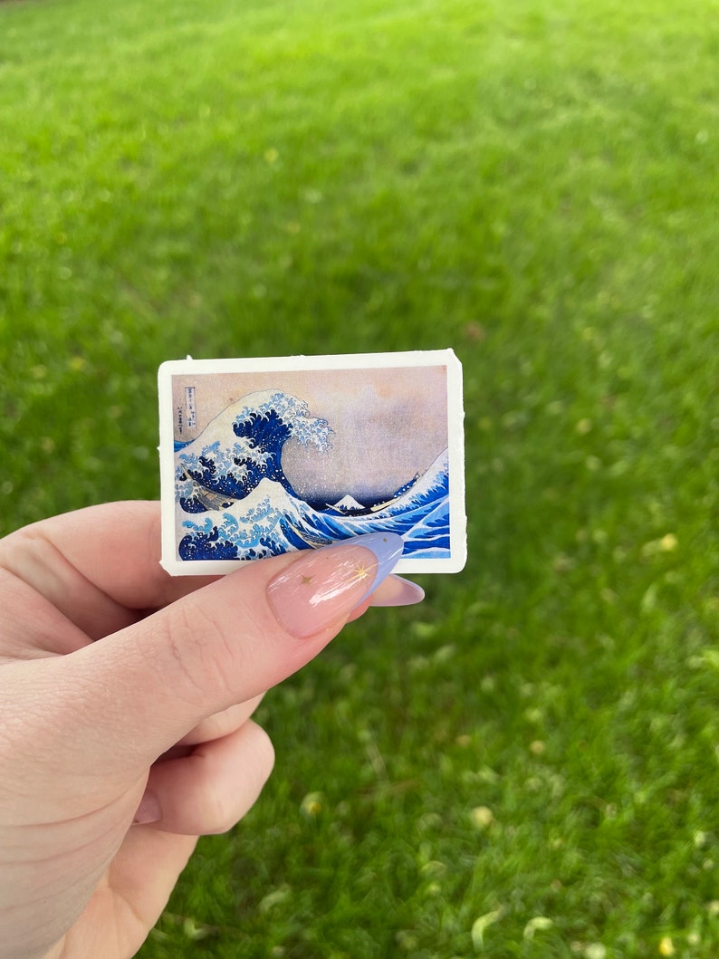 Op de afbeelding: Een sticker met een blauwe en witte afbeelding van de Grote Golf voor Kanagawa, een beroemde Japanse houtsnede van Hokusai.