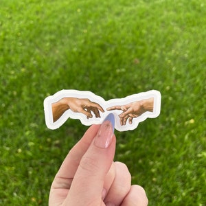 May include: A sticker featuring a recreation of Michelangelo's The Creation of Adam, depicting two hands reaching towards each other.
