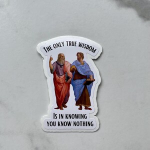 May include: White sticker with a black border featuring two men in Renaissance clothing. The text reads "The only true wisdom is in knowing you know nothing."