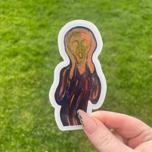 Puede incluir: Una pegatina con la ic&oacute;nica obra de arte de Edvard Munch, "El Grito". La pegatina representa una figura con la boca muy abierta y las manos en la cara, en tonos naranja, rojo y azul. La pegatina tiene un borde blanco y se sostiene sobre un fondo de hierba verde.