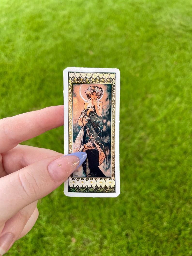 May include: A sticker featuring a vintage illustration of a woman standing in a forest with a crescent moon behind her. The woman is wearing a long, flowing dress with a floral pattern. The sticker has a white background with a gold border.