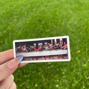 May include: A sticker featuring a reproduction of Leonardo da Vinci's painting "The Last Supper". The sticker shows Jesus and his disciples gathered around a table.