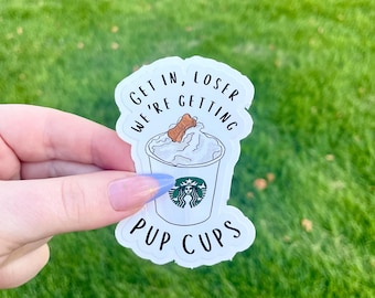 May include: White sticker with the text "Get in, loser we're getting pup cups" and a cartoon image of a Starbucks cup with whipped cream and a dog bone on top.