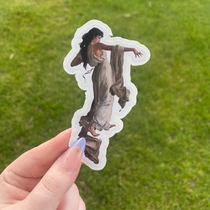 May include: A white sticker with a vintage illustration of a woman in a flowing white dress. The woman is standing on a rock and has her arm outstretched.
