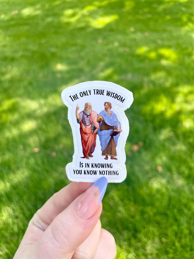 May include: White sticker with a black border featuring a painting of two men. The text reads "The only true wisdom is in knowing you know nothing."