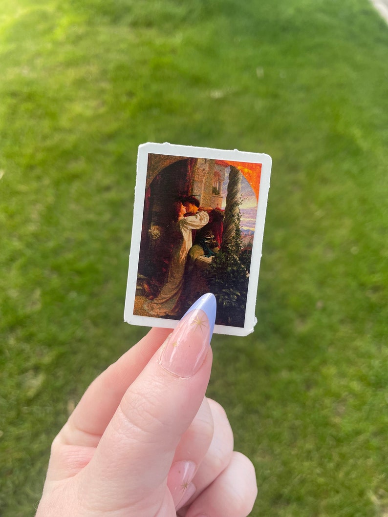 May include: A vintage sticker featuring a painting of a couple embracing in a romantic setting. The painting is set against a backdrop of a stone building and a lush garden. The couple is dressed in period clothing and the colors are warm and inviting.