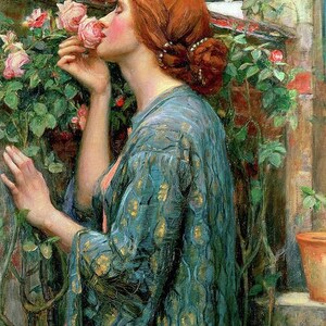 May include: A woman with long red hair is wearing a blue and gold patterned robe. She is smelling a pink rose in a garden setting.