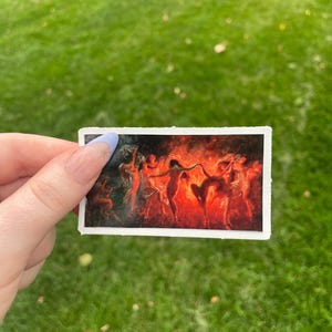 May include: A vintage sticker featuring a painting of a group of people dancing around a fire. The people are nude and the fire is a bright orange and red.