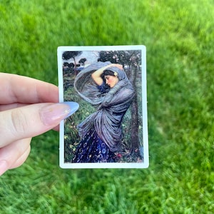 May include: A sticker featuring a painting of a woman in a blue dress and shawl, standing in a field with trees in the background.