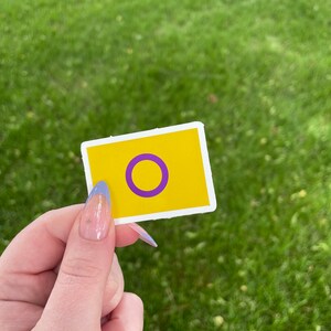 May include: A yellow square sticker with a purple circle inside. The circle is outlined in white.