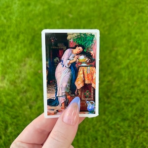 May include: A vintage sticker featuring a painting of a woman in a white dress, leaning on a table with a bowl of fruit. The woman has long dark hair and is looking at the viewer. The background is a dark room with a window and a plant.