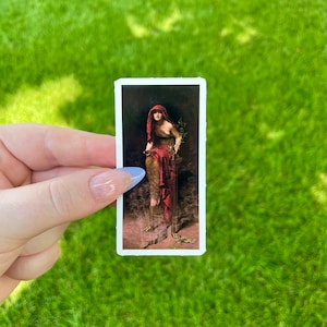 May include: A vintage sticker featuring a painting of a woman in a red robe holding an olive branch. The woman is standing on a pedestal with a broken chain at her feet.