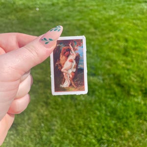 Op de afbeelding: Een sticker met een vintage schilderij van een stel dat elkaar omarmt in een bosrijke omgeving. Het schilderij is in romantische stijl met warme kleuren en een zachte, dromerige sfeer.