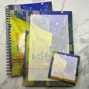 May include: Two spiral bound notebooks with a starry night scene printed on the covers. The smaller notebook is on top of the larger notebook. Both notebooks have a white border around the image.